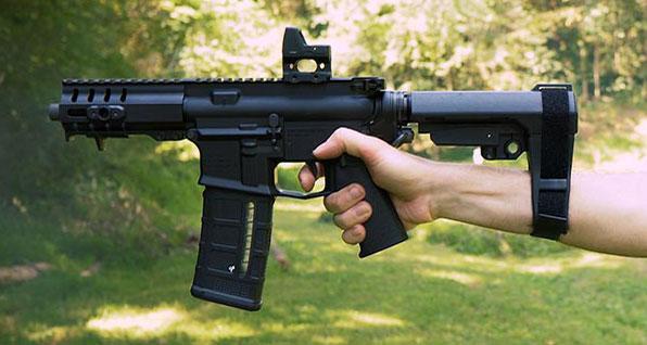 A handgun is shown with a pistol brace extending from a hand and an arm.